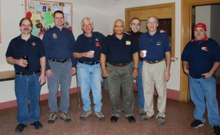 Six people in navy shirts standing indoors at a casual gathering.