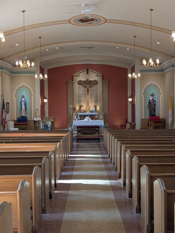 Church interior with wooden pews leading to an altar beneath arched ceiling and hanging lights