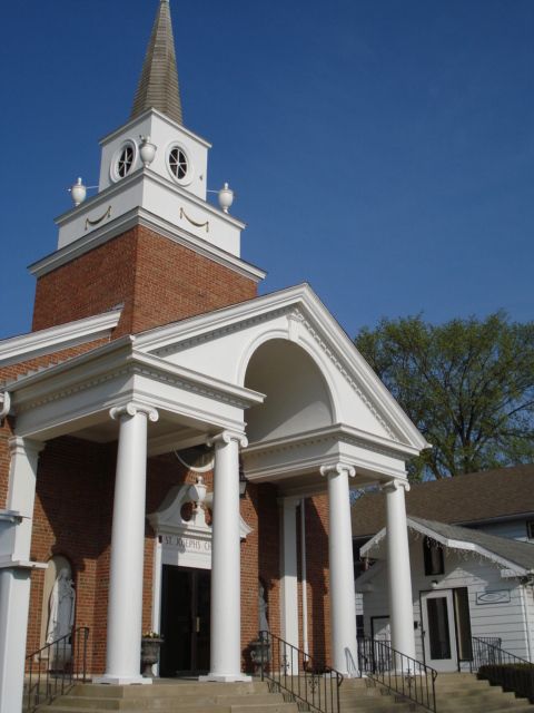 Red brick church with white columns and steeple against a blue sky