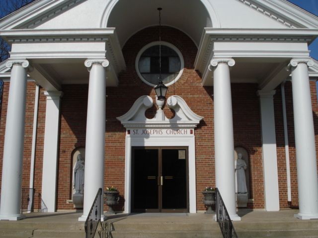 Front entrance of a brick church with white columns, arched doorway, and steps leading to double doors.