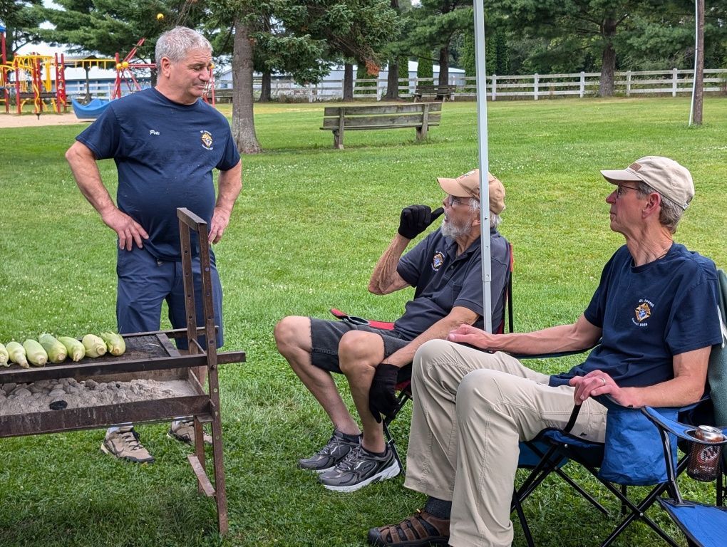 Three men chatting by a croquet court in a park, with croquet balls lined up on the grass.