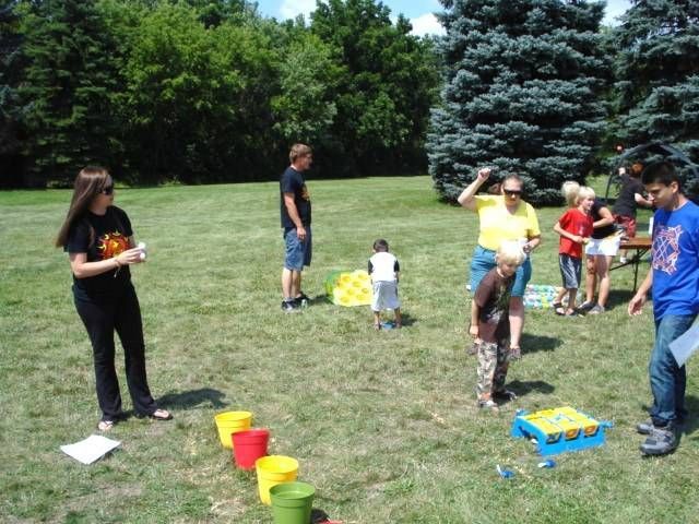 People playing an outdoor game on a grassy field with colorful buckets and a blue toy cart