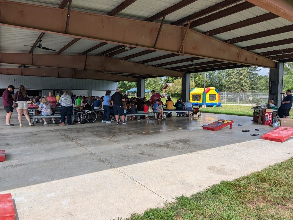 People seated at picnic tables under a pavilion, with inflatable bounce houses in the background.