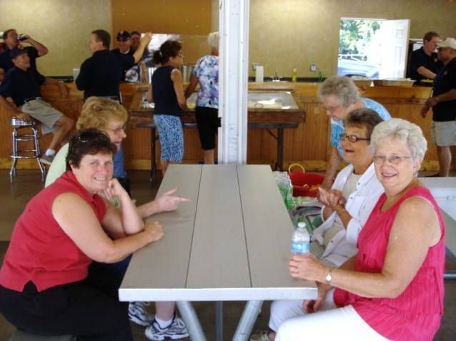 People seated at a table in a bright community hall, with others mingling in the background.