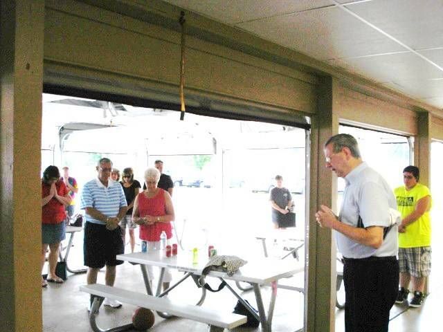People gathered around tables inside a bright open garage or pavilion.