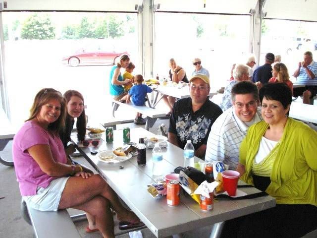 People seated at a picnic table in a bright open-air pavilion, eating and talking with drinks and snacks.
