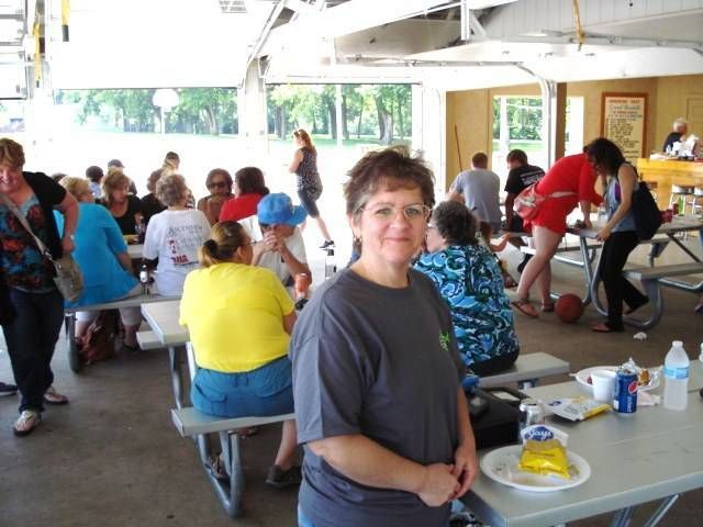 People sitting at picnic tables in a covered outdoor pavilion, with a woman smiling in the foreground.