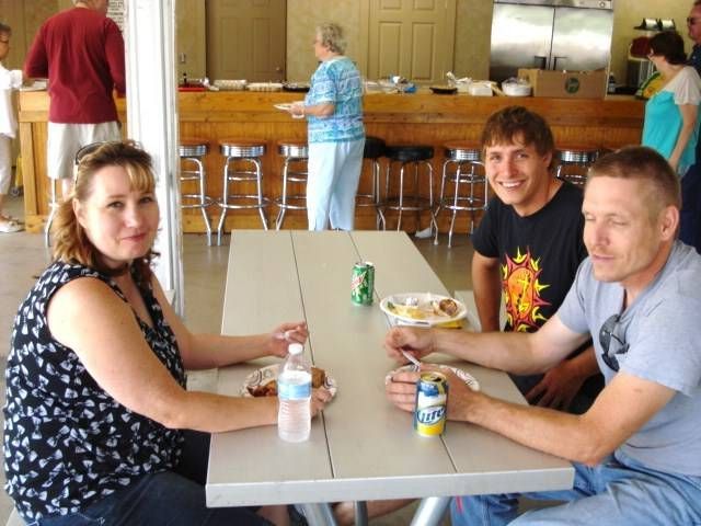 Three people sitting at a cafeteria table with drinks and food, smiling toward the camera.