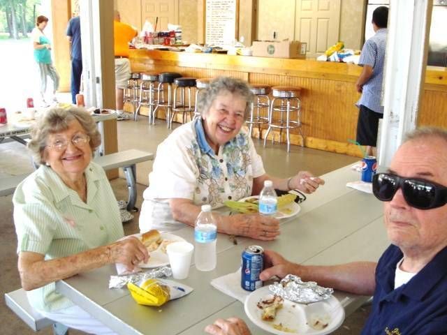 Three people dining at a bright cafeteria table, with trays, drinks, and a wooden counter in the background