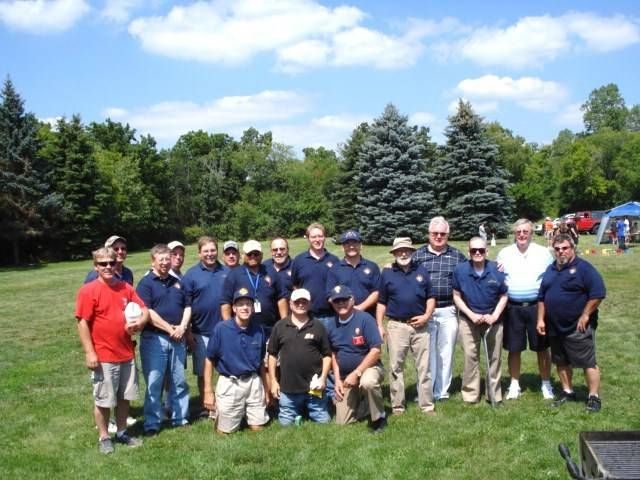 Group of people posing on a grassy field with trees and blue sky in the background