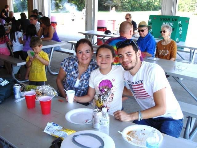 Family seated at a picnic table, smiling at a covered outdoor picnic area with red cups and plates