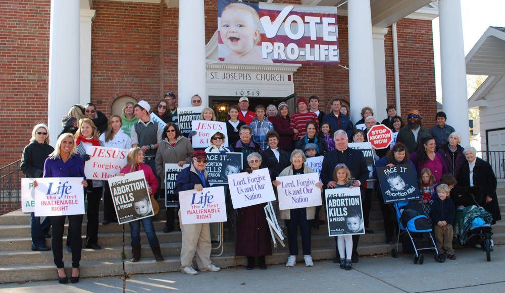 Group of people holding “Vote Pro-Life” signs on church steps during a rally