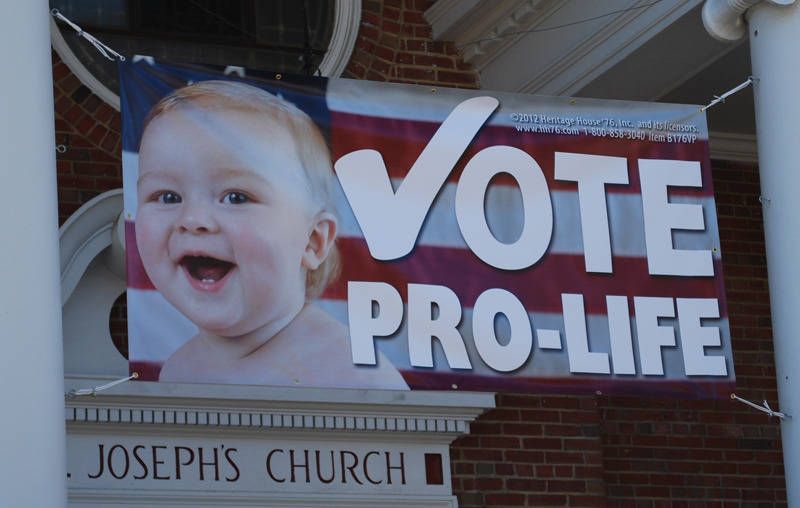 Pro-life campaign banner with baby photo and “VOTE PRO-LIFE” on a church building