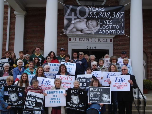Pro-life group posing outside church with signs protesting abortion, beneath a large 40 Years banner