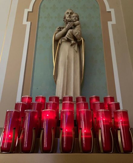 Statue of a saint holding a child above rows of red votive candles