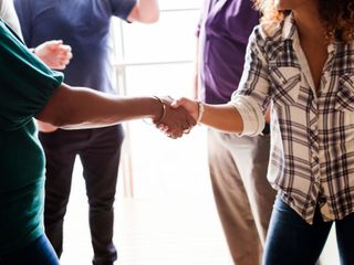People shaking hands in a bright office, with others standing nearby in the background.