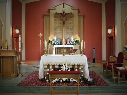 Church altar with white cloth, candles, flowers, and red walls in a sanctuary