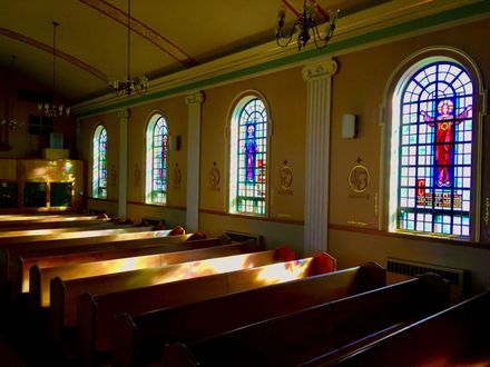 Sunlit church interior with wooden pews and colorful stained glass windows