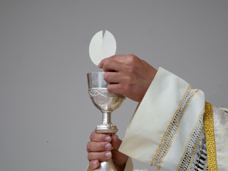 Priest holding a silver chalice and communion wafer during a church service