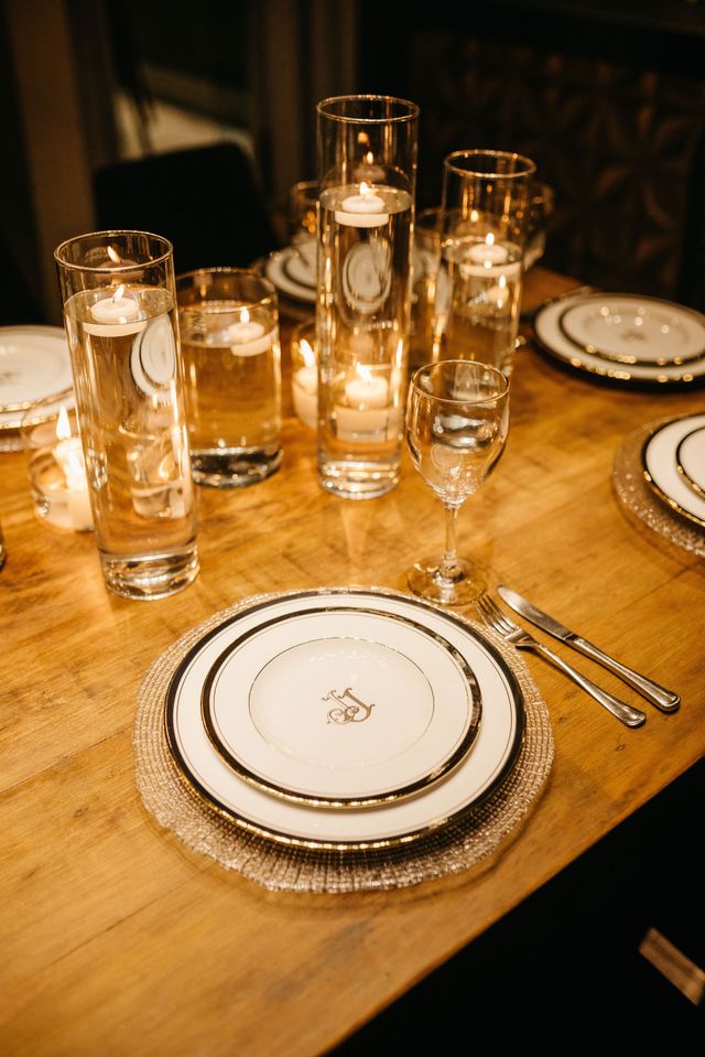 Set dining table with white plates, silverware, candles, and tall glasses on a wooden table.