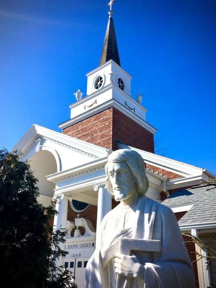 White statue in front of a red-brick church with a white steeple under a blue sky