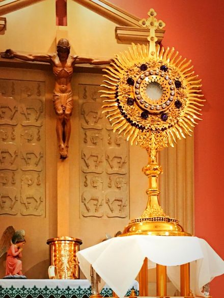 Golden church monstrance on altar beside crucifix, draped in white cloth
