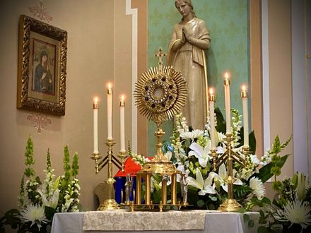 Catholic altar with candles, white lilies, and a statue of a saint against a green wall