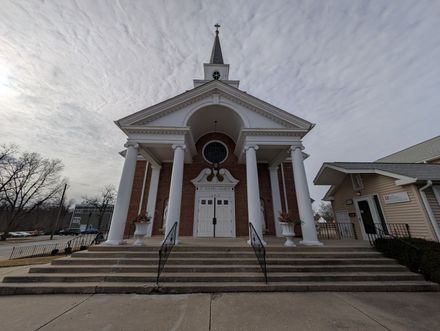 White church with tall columns and steeple, viewed from steps under a cloudy sky