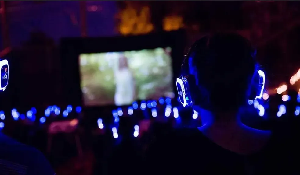 A group of people wearing headphones watching a movie outside under the stars