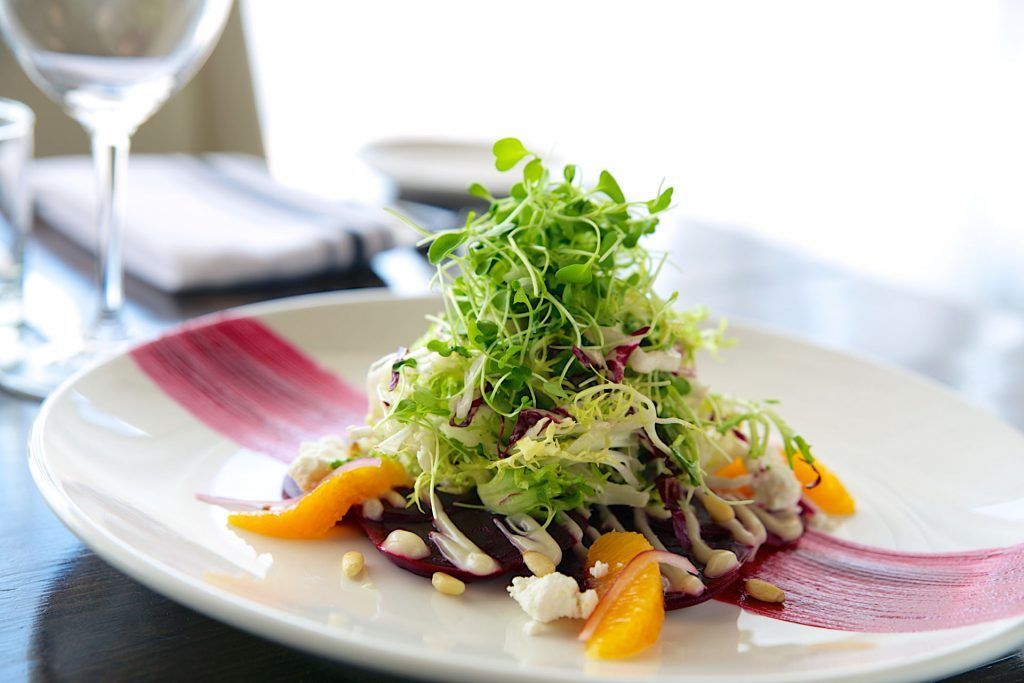 A white plate topped with a salad and a glass of wine on a table.