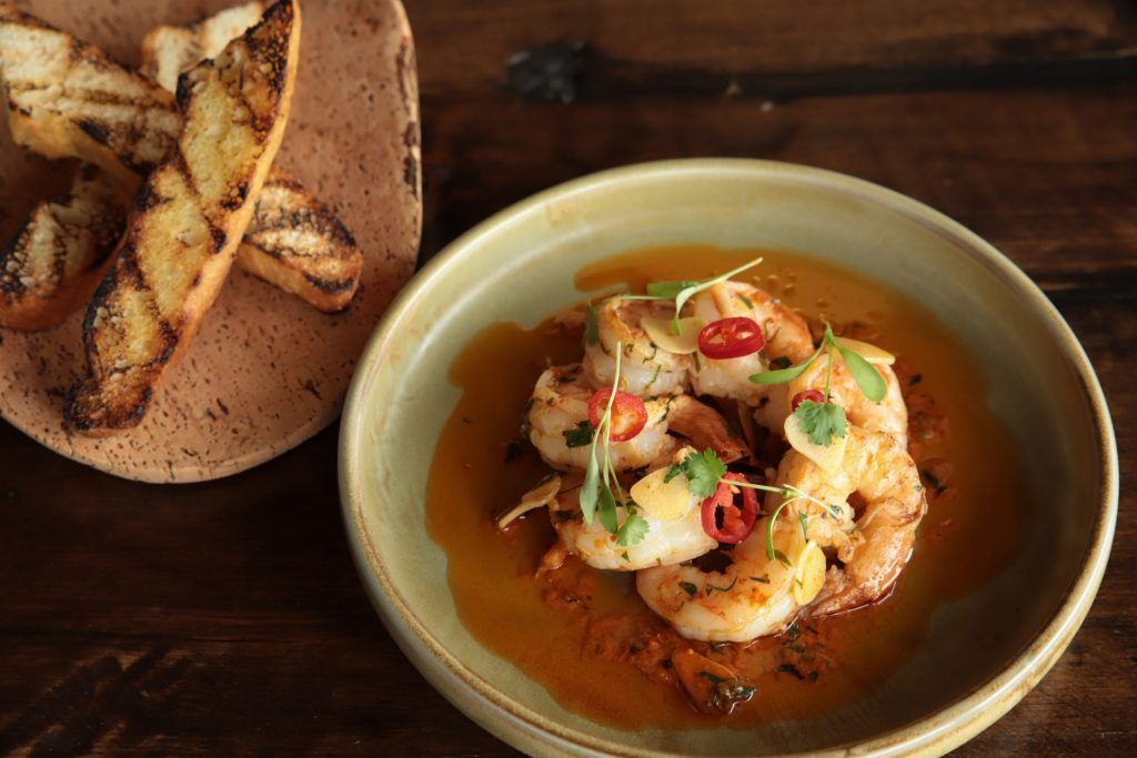 A bowl of shrimp next to a plate of french fries on a wooden table.