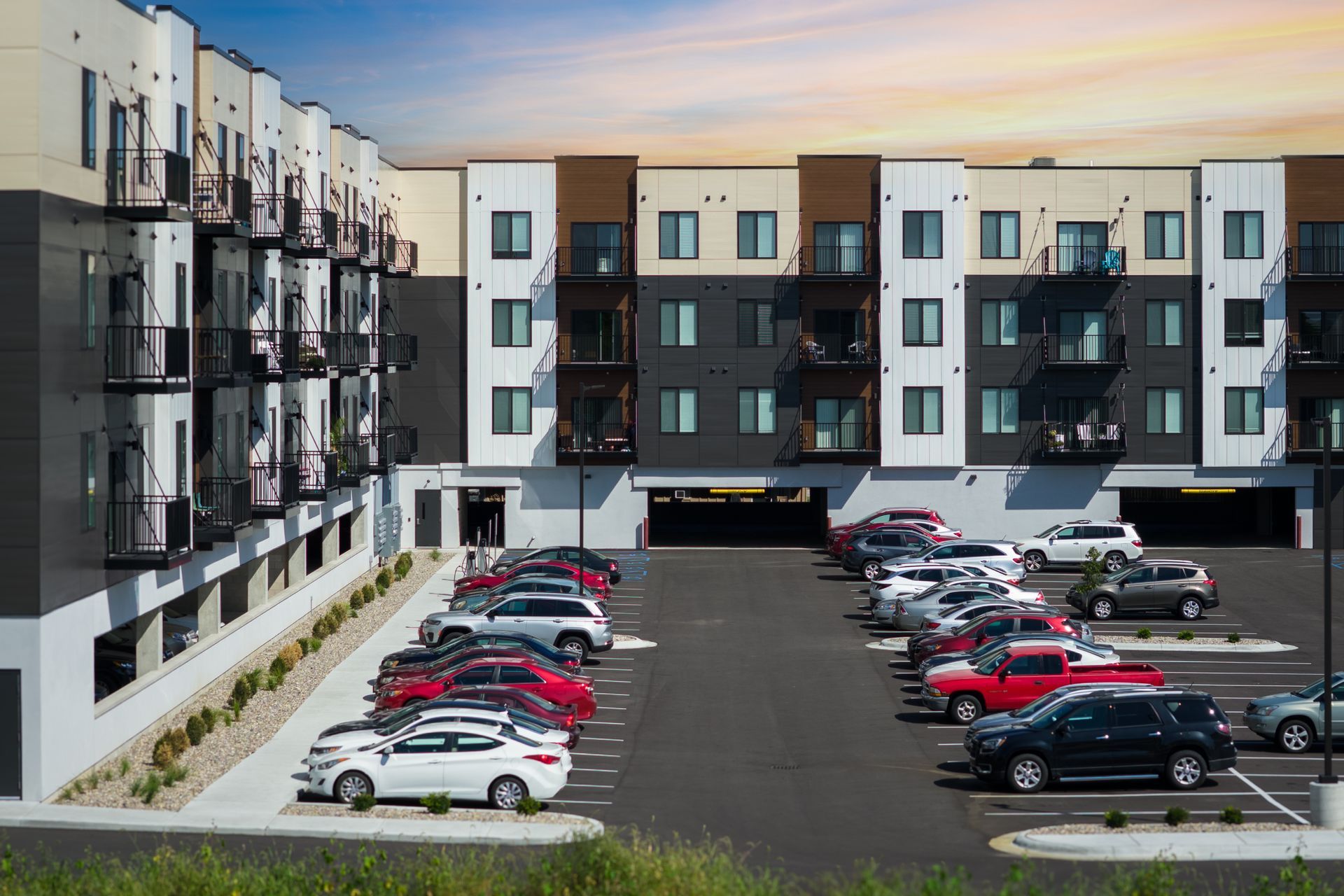Apartment building with cars parked in front of a partially covered parking garage.