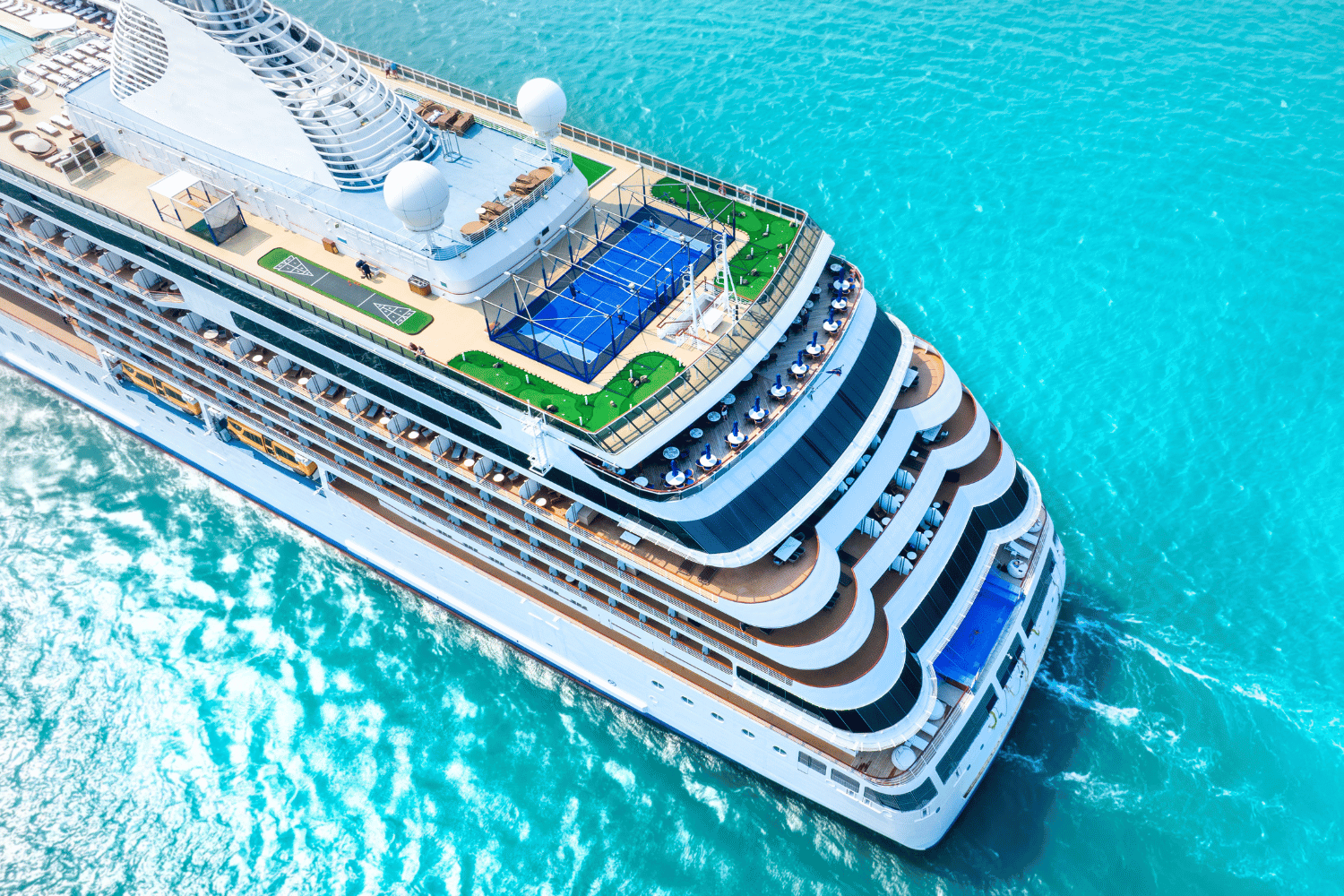 Aerial view of a large white cruise ship sailing through bright turquoise water