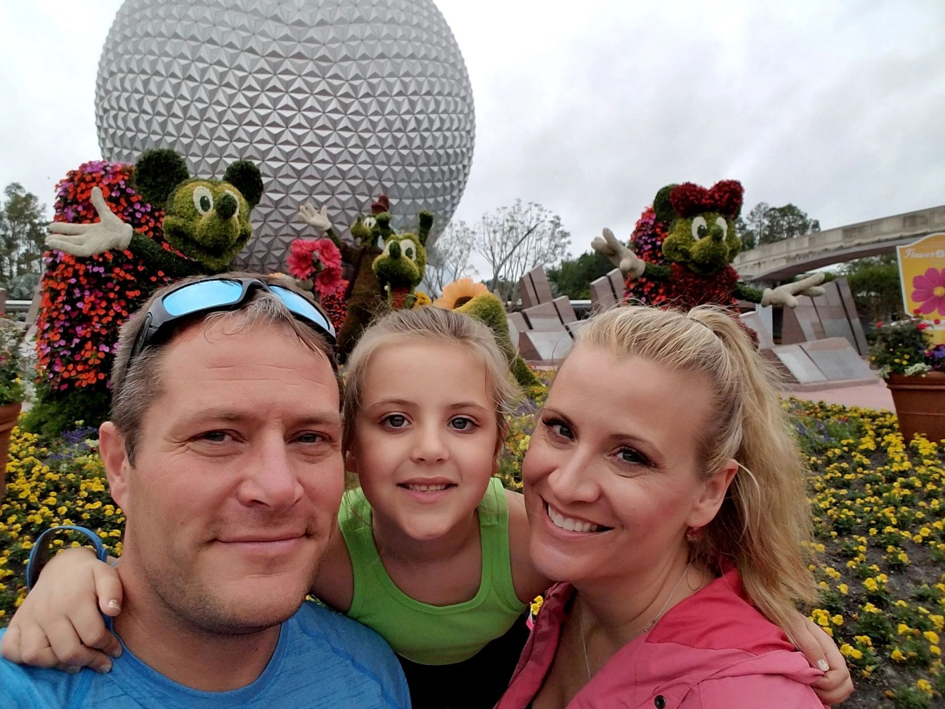 Three people smiling in a flower garden with a large geodesic sphere behind them