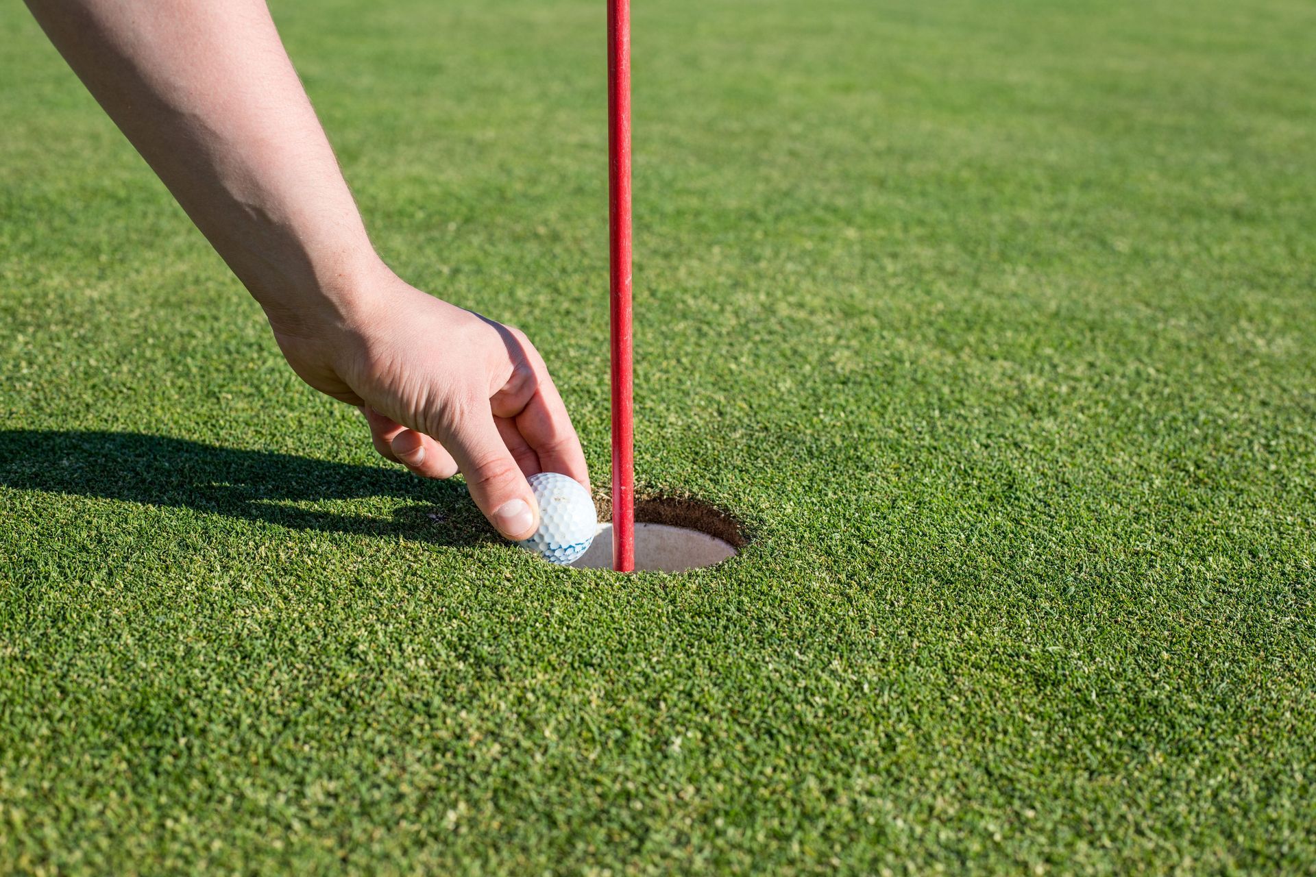 Hand placing a golf ball beside the hole on a green putting surface