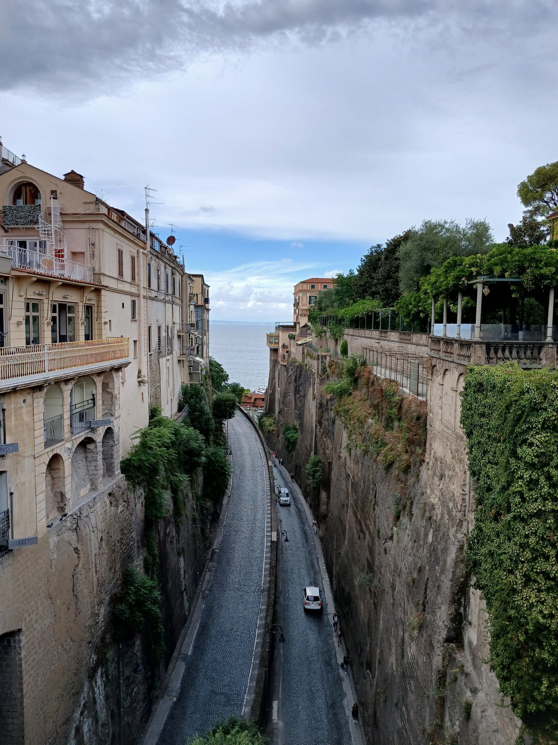 Narrow river gorge between old stone buildings and cliffs, with a road below and trees on the right.