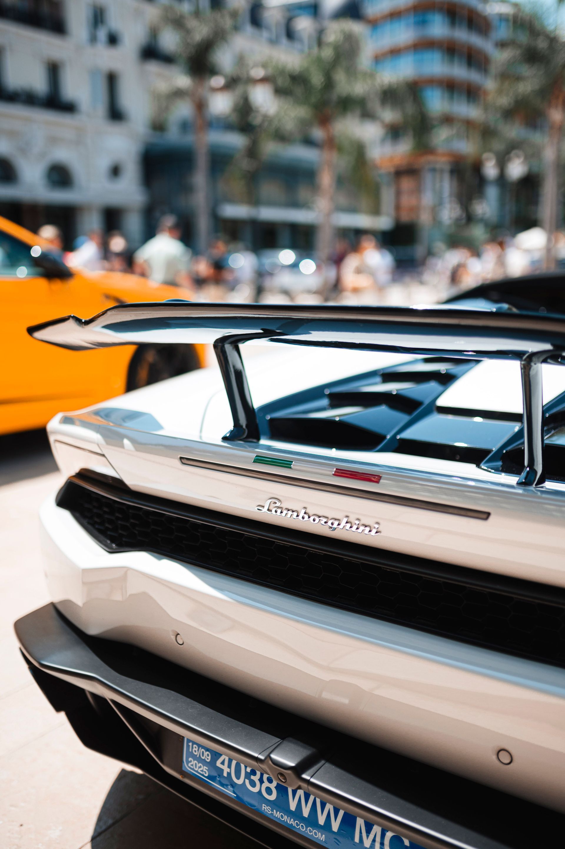 Rear view of a cream Porsche sports car at an outdoor event, with orange barriers and blurred city background