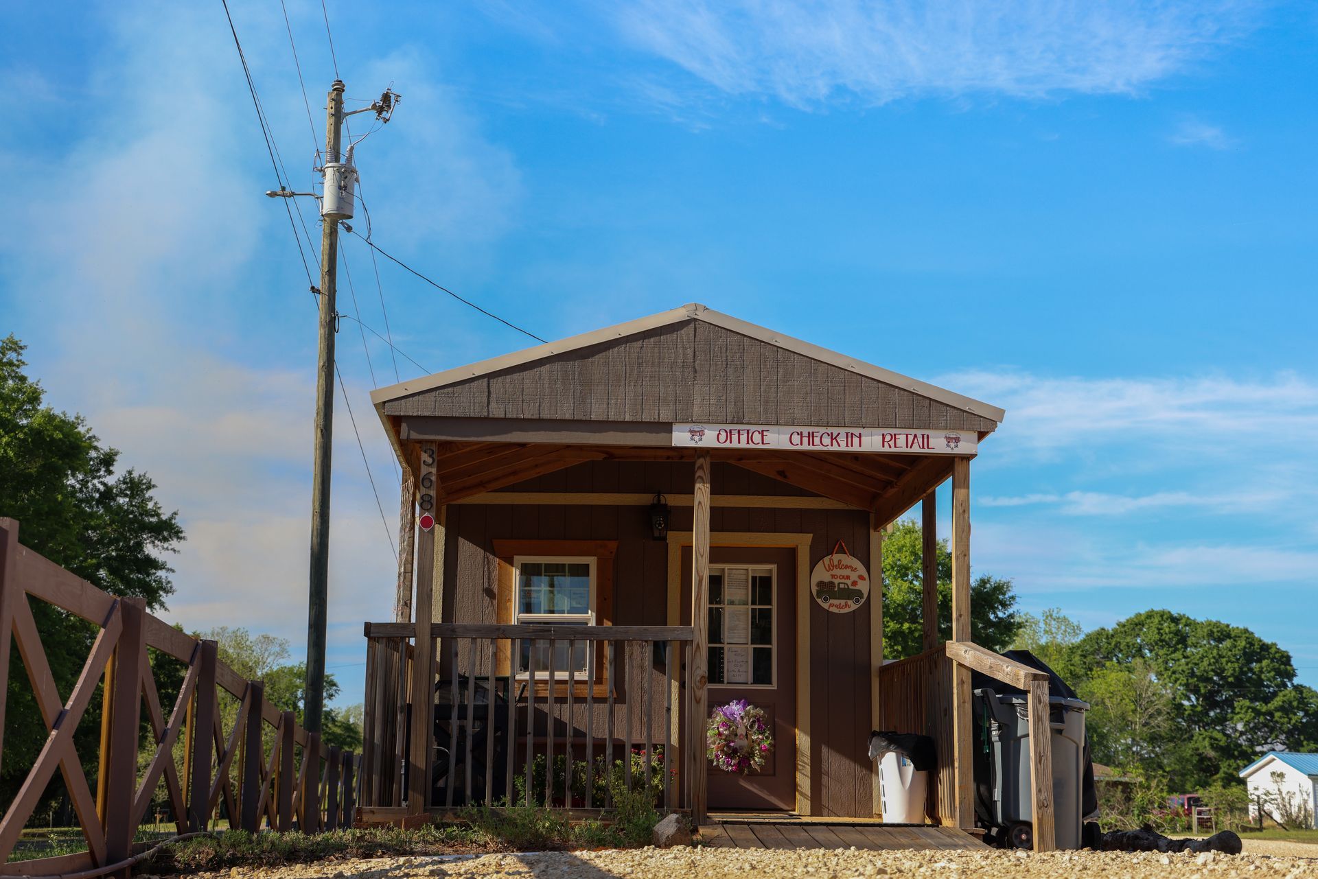 Small rustic wooden house with a porch, under a blue sky, beside a fence and utility pole.