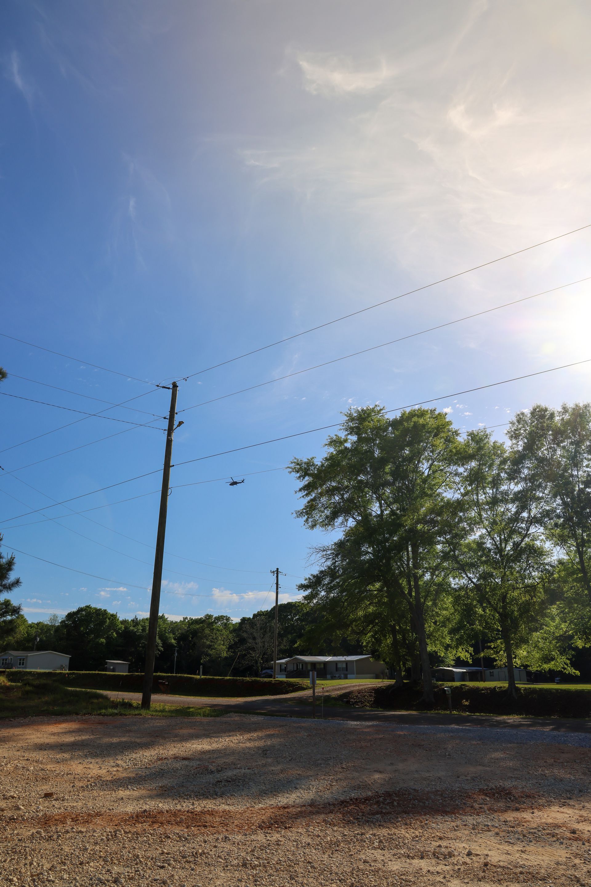 Sunny sky over a gravel lot with power lines, trees, and a wooden pole.