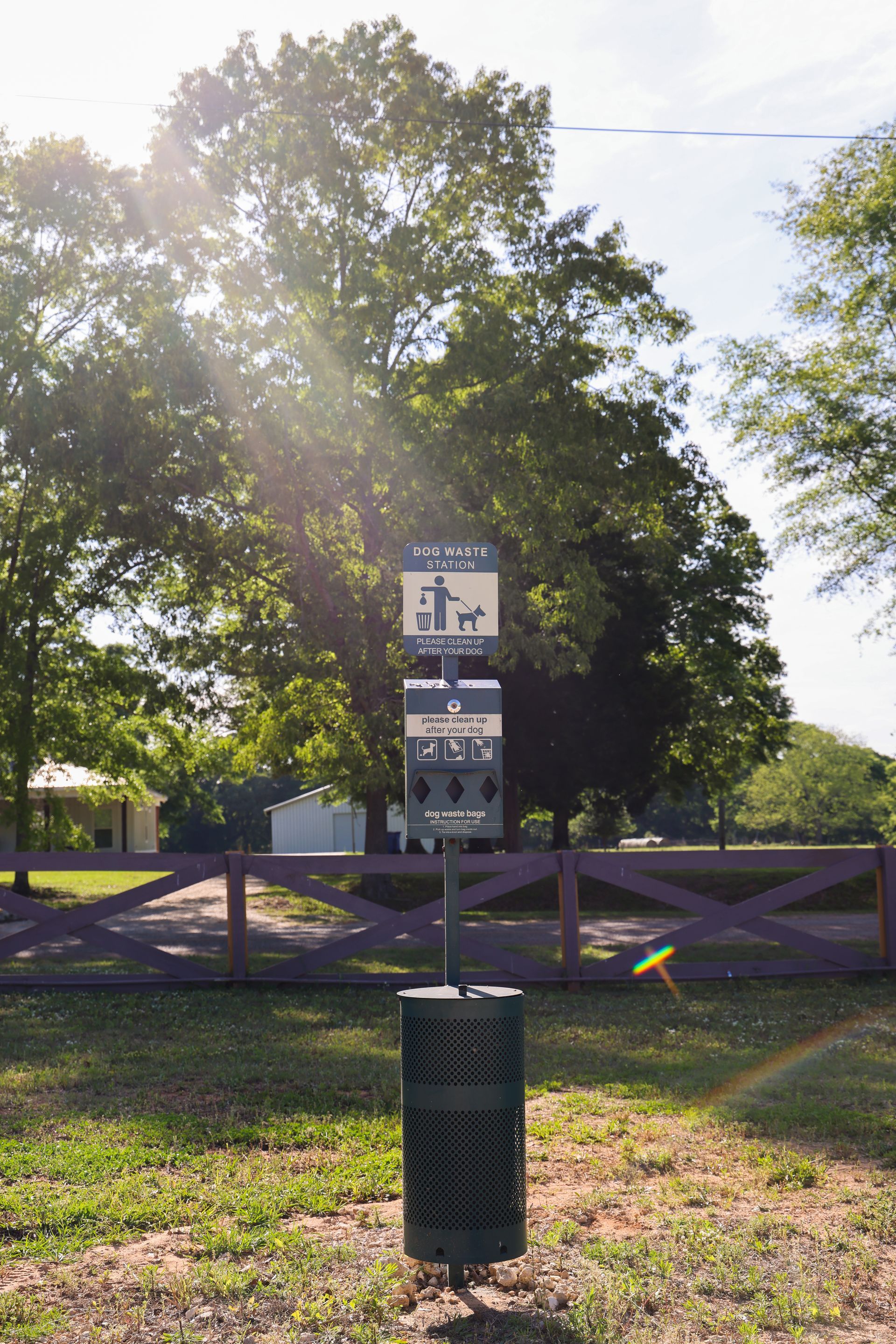 Trail sign beside a wooden fence in a sunny park with trees and grass