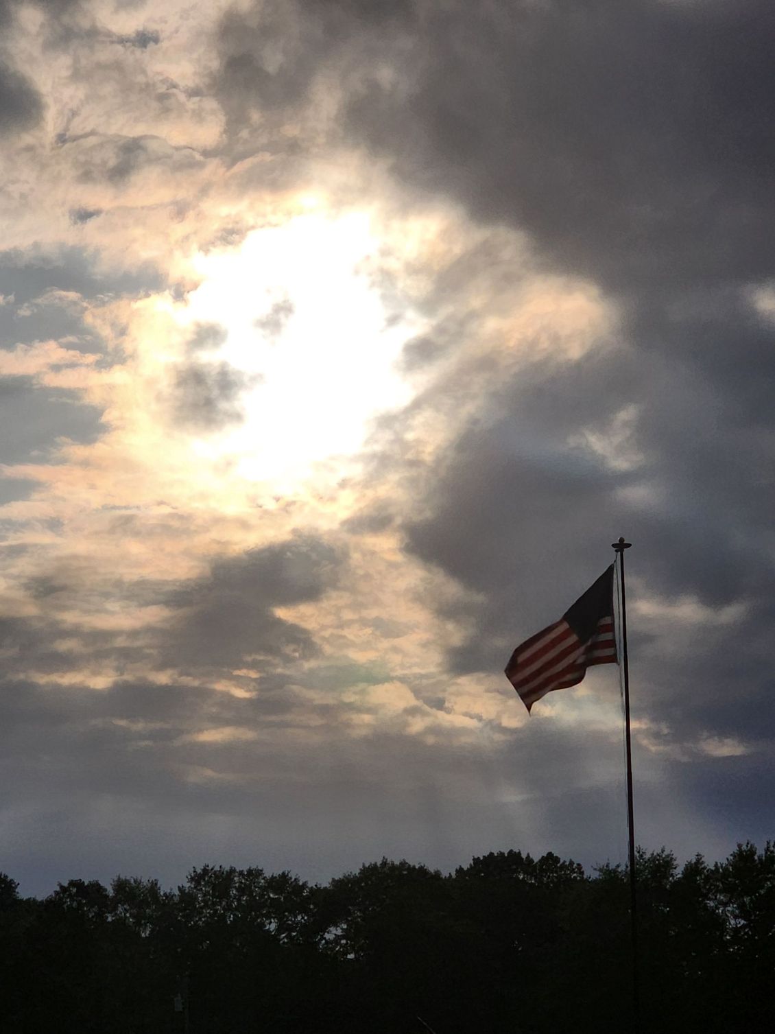 American flag on a pole against a cloudy sunset sky over trees