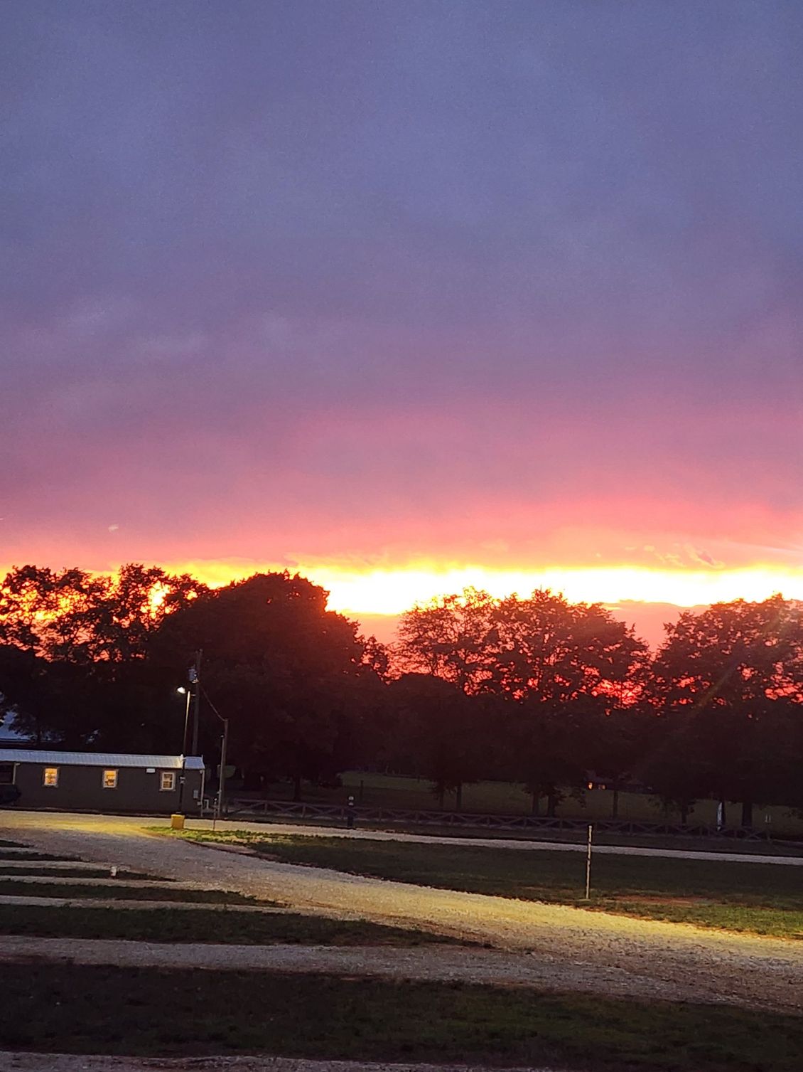Sunset over silhouetted trees and a small building, with a glowing pink and orange horizon