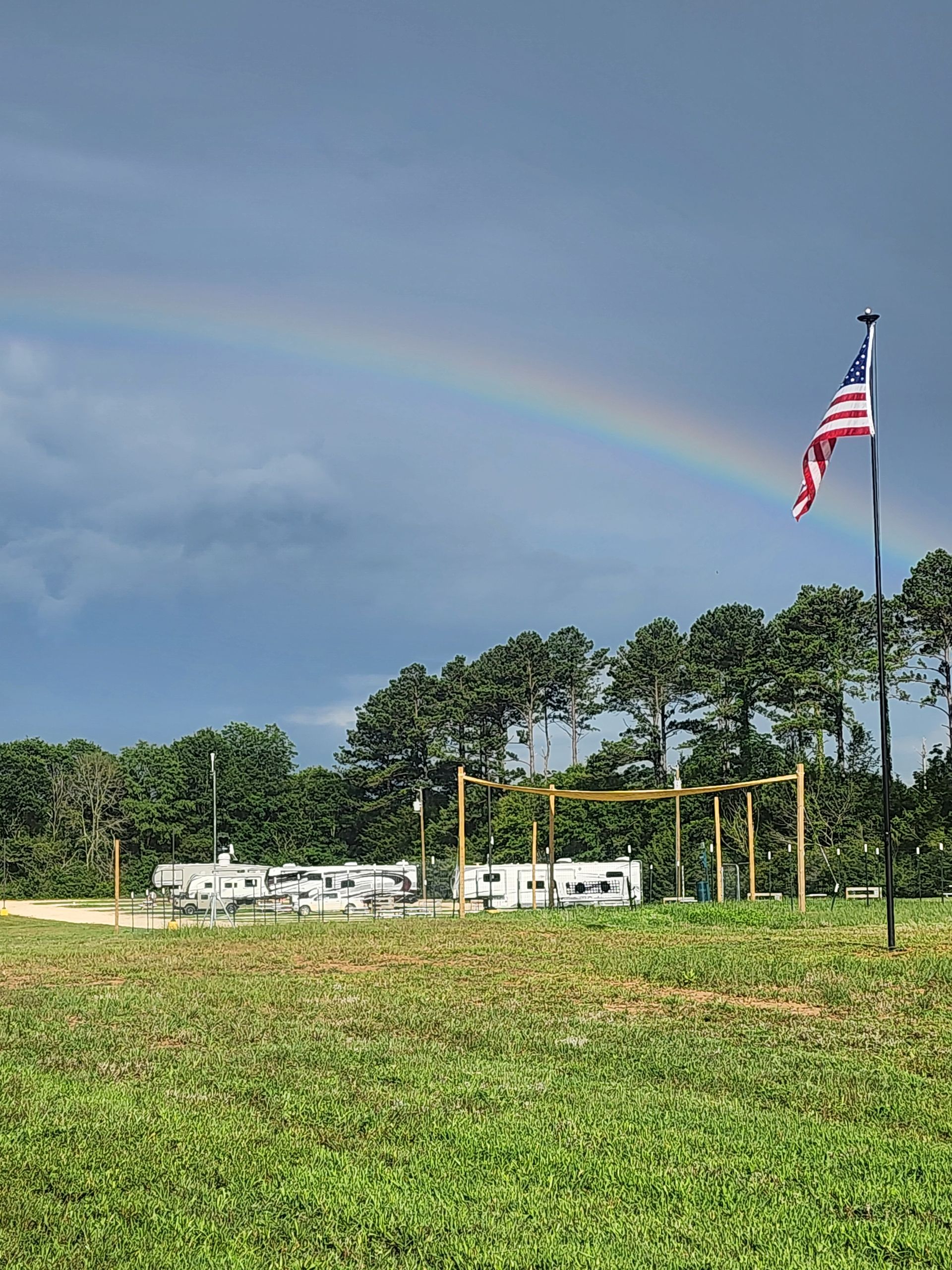 Rainbow over a grassy field with a U.S. flag on a pole and white RVs in the distance.