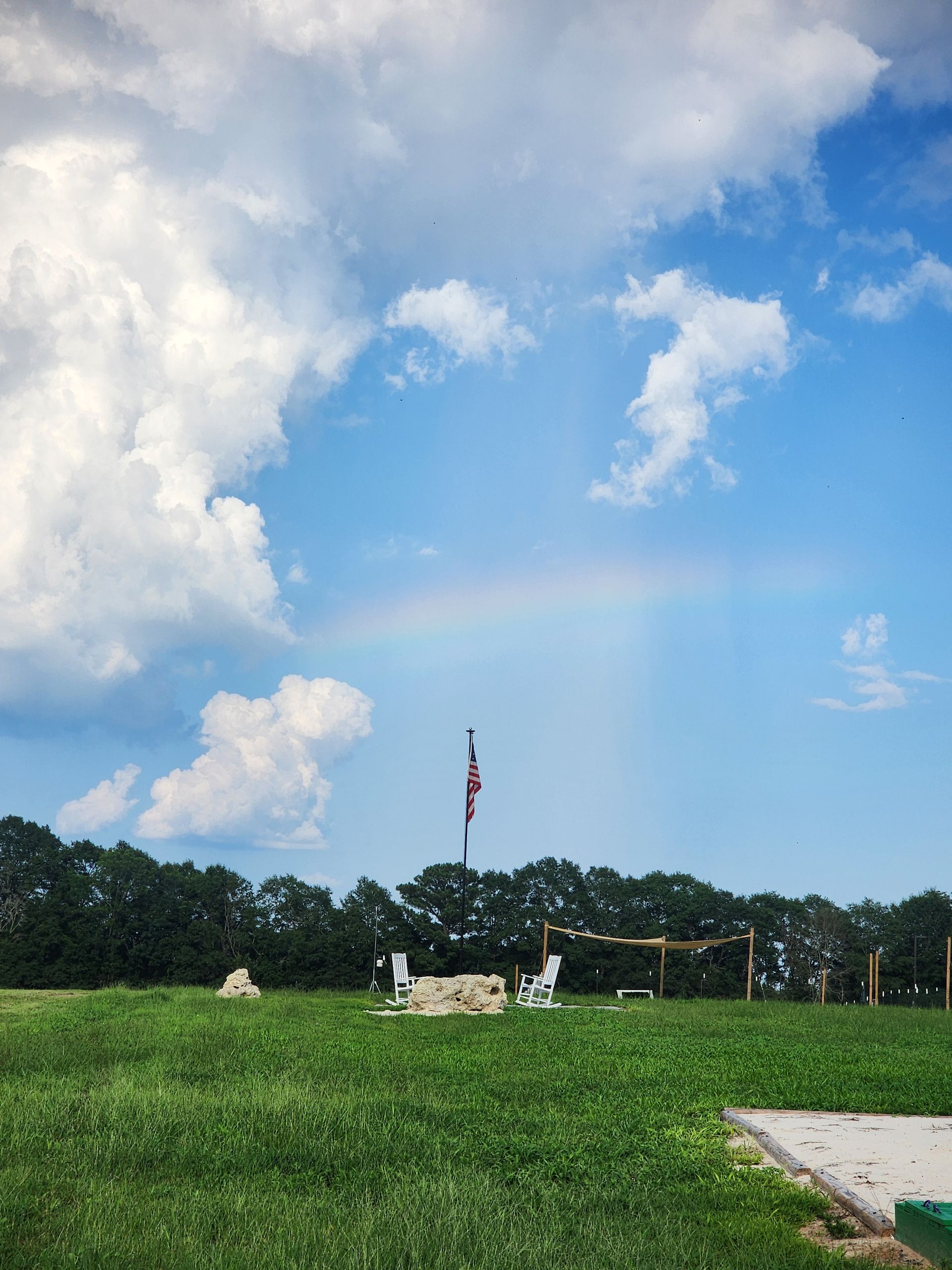 Grassy field under a blue sky with clouds and a distant American flagpole