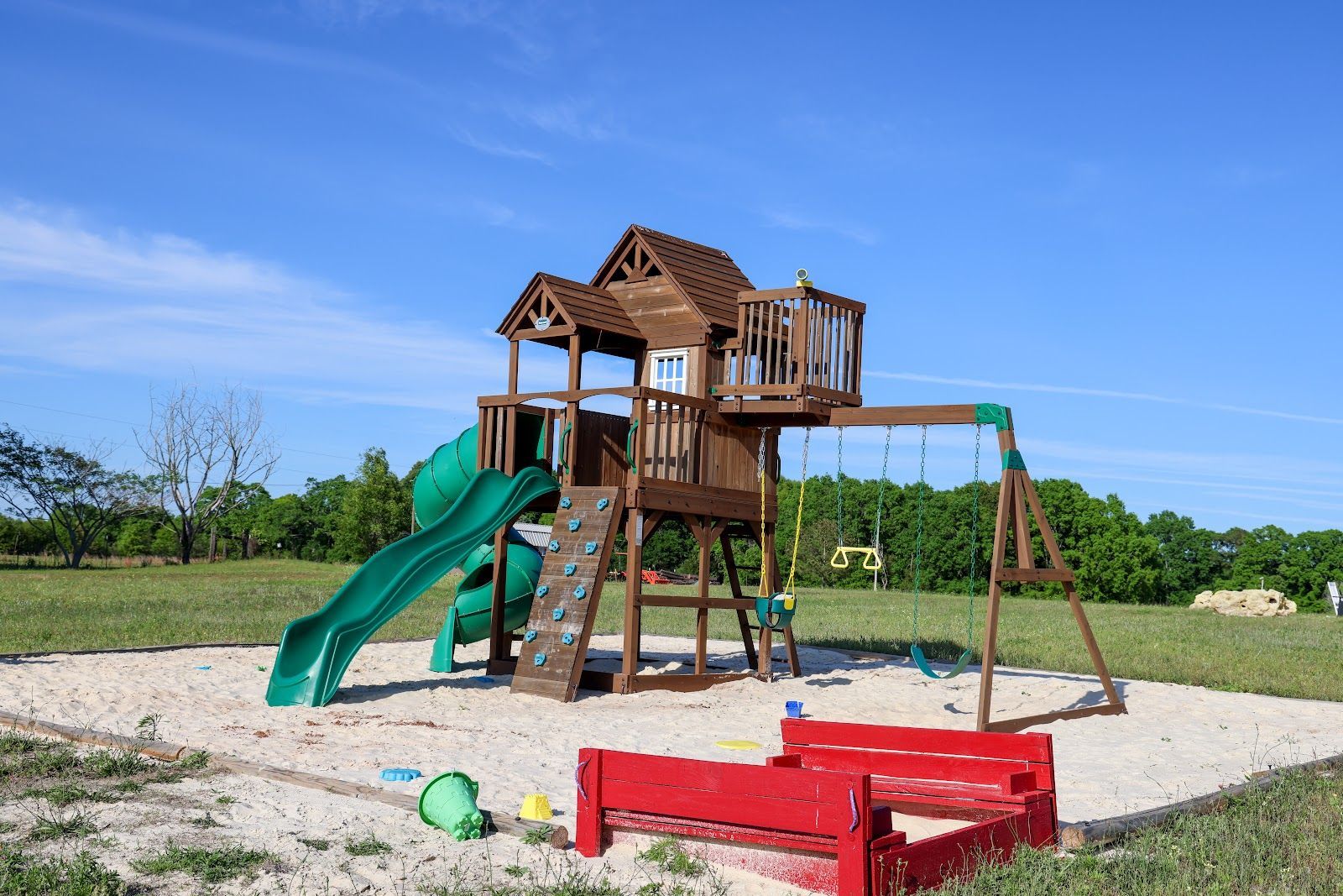 Wooden playground tower with green slides and swings in a sunny park with sand and grass