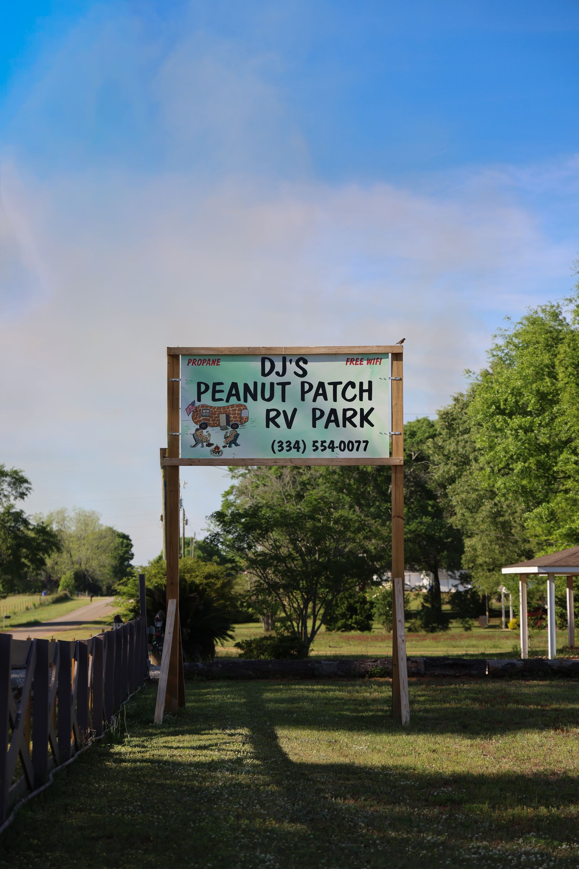 Entrance sign for DJ’s Peanut Patch RV Park on a sunny day, with a fence and trees nearby