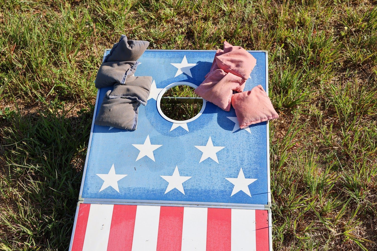 Patriotic cornhole board on grass with star-spangled design and bean bags on top