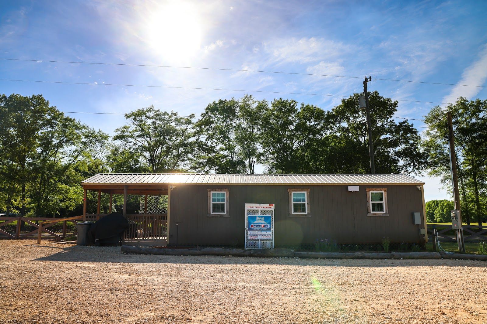Small brown building with a covered porch and sign, set on a gravel lot under a bright blue sky.