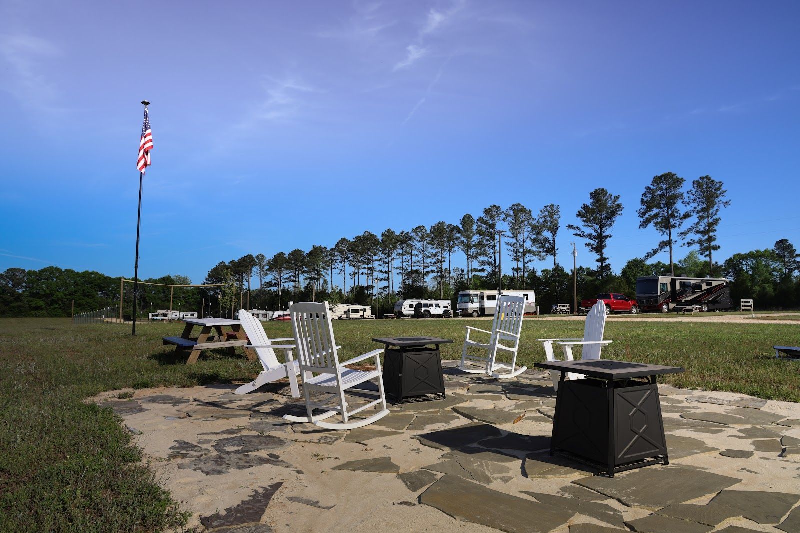 Outdoor patio with white chairs and tables on a concrete pad beside a grassy field and flagpole.