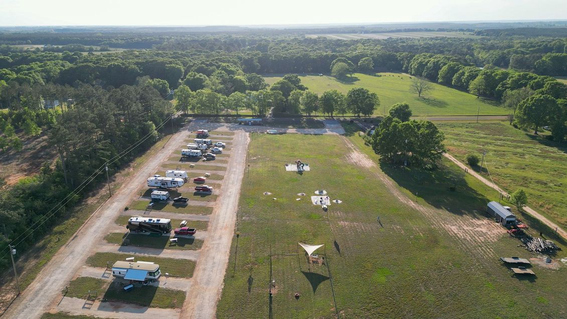Aerial view of a rural event field with parked cars, tents, and open grassy areas beside trees